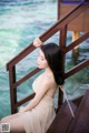 A woman in a beige dress sitting on a wooden railing.