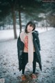 A woman standing in the snow wearing a scarf and jacket.