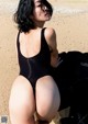 A woman in a black bathing suit sitting on a rock.