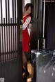 A woman in a red dress standing next to a suitcase.