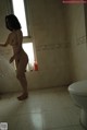 A naked woman standing in a bathroom next to a toilet.