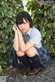 A young woman in a school uniform sitting on the ground.