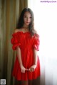 A woman in a red dress posing by a window.