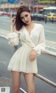 A woman in a white dress leaning against a railing.