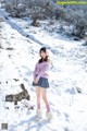 A woman in a pink sweater and skirt standing in the snow.