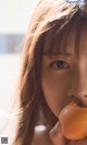 A woman holding a peach in front of her mouth.